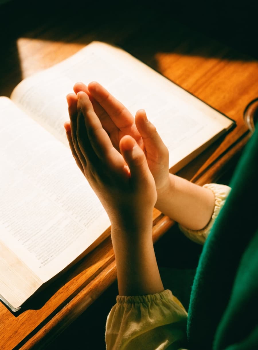 Mains d'enfant levées en invocation au-dessus d'un livre